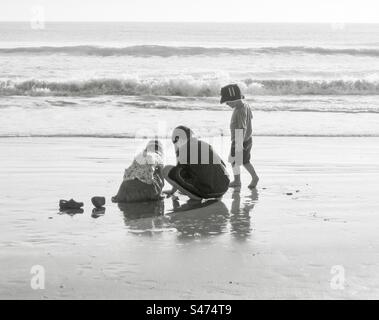 Trois enfants jouant sur une plage en noir et blanc. Banque D'Images