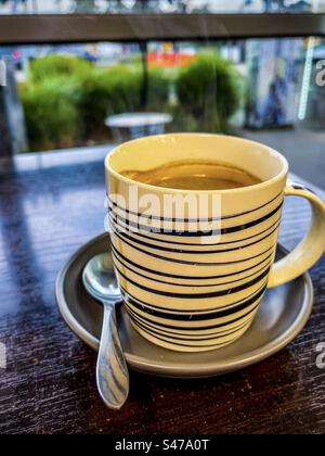 Gros plan de café chaud à la vapeur dans une tasse et une soucoupe sur la table devant une fenêtre dans le café. Rafraîchissement. Boisson chaude. Banque D'Images
