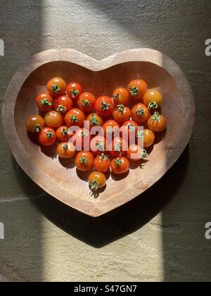 Bol en bois en forme de coeur avec tomates cerises cultivées maison dans un puits de lumière du soleil Banque D'Images