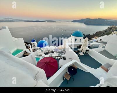 Vue sur la caldeira d'Oia, Santorin et la mer Égée au coucher du soleil avec les célèbres 3 dômes bleus en vue. Banque D'Images