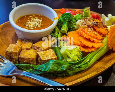 Gros plan de cubes de tofu frits croustillants et de légumes fraîchement cuits à la vapeur avec une sauce aux arachides épicée trempée dans un bol sur une assiette sur la table. Nourriture végétarienne / végétalienne. Manger sainement. Mangez vos couleurs. Banque D'Images