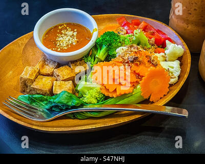 Vue à grand angle de cubes de tofu frits croustillants et de légumes fraîchement cuits à la vapeur avec une sauce aux arachides épicée trempée dans un bol sur une assiette sur la table. Nourriture végétarienne/végétalienne. Manger sainement. Cuisine asiatique. Mangez vos couleurs. Banque D'Images