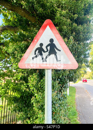 Un panneau routier en forme de triangle avertissant les conducteurs que des enfants traversent la route près d'une école. Banque D'Images