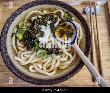 Directement au-dessus, vue rapprochée des nouilles udon dans la soupe miso avec onsen tamago / oeuf poché, algues et graines de sésame dans un bol avec cuillère et baguettes sur plateau en bois Washoku. Cuisine japonaise traditionnelle. Banque D'Images