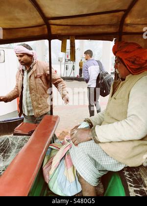 Un homme âgé portant un turban rouge assis à l'intérieur d'un pousse-pousse près d'une pompe à essence Banque D'Images