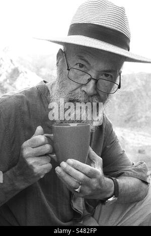 Portrait monochrome de l'homme âgé buvant du café contre les montagnes Banque D'Images