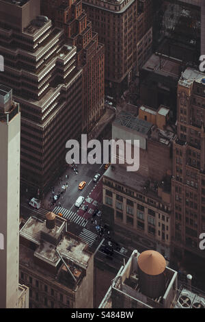 Haut au-dessus de New York City regardant vers le bas entre les grands bâtiments et les gratte-ciel à un coin de rue avec taxi jaune et circulation Banque D'Images