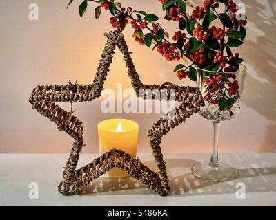 Arrangement de bougies allumées derrière l'étoile décorative en rotin et les branches rouges de baies Cotoneaster en gobelet de cristal. Allumé. Noël. Célébration. Banque D'Images