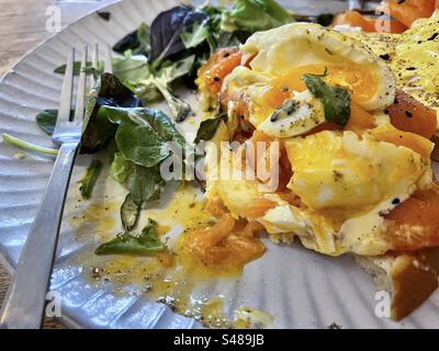 Gros plan d'œufs partiellement mangés Benedict avec saumon fumé, sauce hollandaise et salade de feuilles d'épinards sur l'assiette sur la table. Banque D'Images