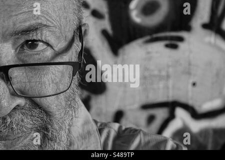 Portrait monochrome de l'homme âgé contre le mur de graffiti Banque D'Images