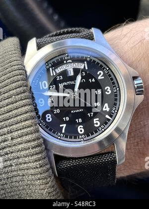 Plan rapproché d'une date Hamilton Khaki montre de style militaire avec cadran noir sur poignet poilu avec un pull sur bracelet en tissu noir OTAN et fond noir Banque D'Images