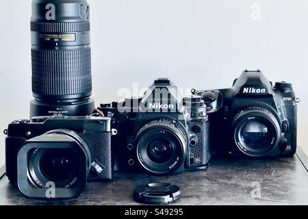 Photo studio de trois appareils photo numériques sur une étagère en bois. Un Fujifilm X-E2S avec ruban adhésif, un Nikon DF et un Nikon D780 avec objectifs assortis et téléobjectif. Banque D'Images