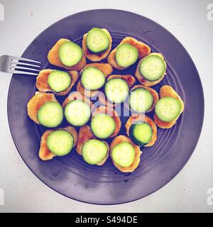 Vue de dessus de l'assiette de nombreuses pépites de poulet frites avec une tranche de concombre vert sur chacune avec afork à proximité teady à manger pour le dîner par la nourriture affamée enfant enfants affamés Banque D'Images
