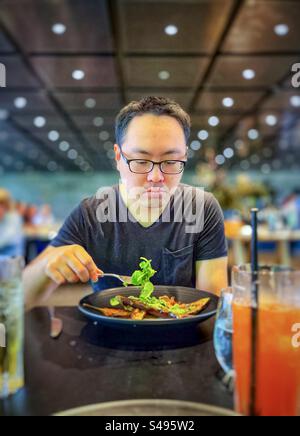 Homme asiatique en lunettes appréciant un repas végétarien de salades fraîches et d'aubergines grillées au miso à table dans le restaurant. Manger sainement. Concentrez-vous sur le premier plan. Banque D'Images