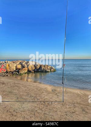 Scène de pêche sereine et calme sur une plage de sable avec barrière rocheuse à Valence, Espagne par une journée ensoleillée d'hiver en décembre. Banque D'Images