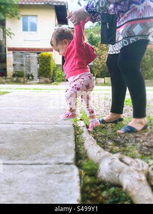 Les premiers pas de bébé à l’extérieur. Bébé marchant avec excitation étant aidé par un adulte Banque D'Images