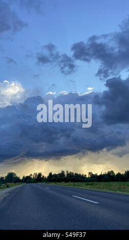 Entre la pluie et les orages marchant sur une route asphaltée rurale en Lettonie. Nuages très sombres un jour d'été en Lettonie avec un peu de pluie des nuages. Les orages sont à proximité. Banque D'Images