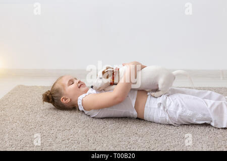 Les enfants, les animaux et les chiens concept - petite fille adorable Enfant allongé sur le sol et jouer avec drôle chiot Jack Russell Terrier Banque D'Images