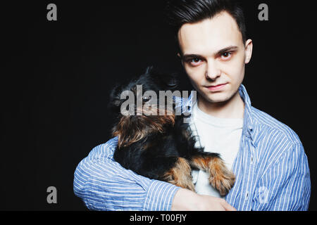 Closeup portrait beau jeune homme hipster et son bon ami chien noir sur fond noir. Des émotions positives, expression du visage, les sentiments. C Banque D'Images