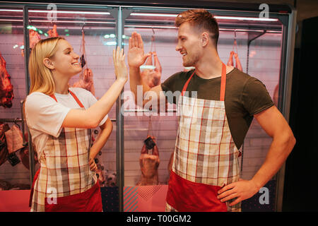 Jeune homme et femme se tenir à table étagère en épicerie. Ils donnent à chaque haut-cinq autres et sourire. Les travailleurs heureux de poser. Banque D'Images