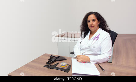 Latin féminin female doctor sitting with attitude sérieuse dans son bureau avec stéthoscope sur son cou sur fond blanc Banque D'Images