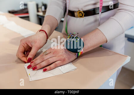 Les mains avec un chiffon sur mesure, le motif et l'aiguille dans l'atelier Banque D'Images