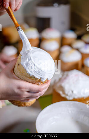 Brosses d'un boulanger un liquide sucre fouettée cerise sur le sommet d'un gâteau de Pâques traditionnel fabriqué à partir de pâte et cuit dans des formes cylindriques pour décorer les t Banque D'Images
