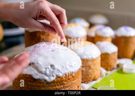 Baker décore la partie supérieure de Pâques gâteaux couverts de glaçage en sucre blanc sucre cristallisé coloré décoration verser sur les décisions de givrage tra Banque D'Images