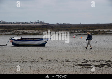 Randonneur femme marchant vers un bateau sur la plage à marée basse à St Clement Bay sur l'île de Jersey, Îles britanniques, Royaume-Uni. Banque D'Images