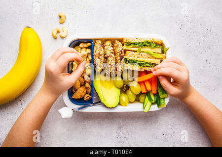 School healthy lunch box avec sandwich, des biscuits, des noix, des fruits et de l'avocat sur un fond blanc. Banque D'Images