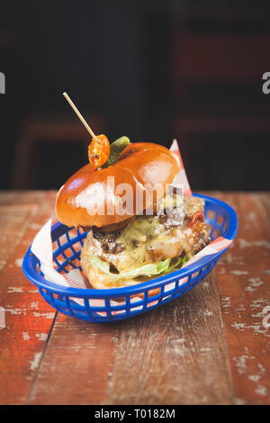 Burger de boeuf gras dans un petit pain brioché servi dans un panier bleu sur une table en bois Banque D'Images