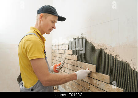 L'installation des carreaux sur le mur. Le travailleur de mettre des tuiles dans la forme de brique. Banque D'Images