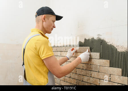 L'installation des carreaux sur le mur. Le travailleur de mettre des tuiles dans la forme de brique. Banque D'Images