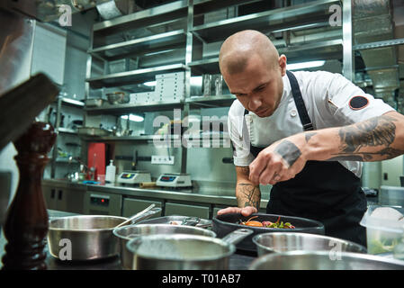 Travail délicat. Célèbre chef confiant avec plusieurs tatouages sur ses bras de garnir les pâtes à la Carbonara dans une cuisine de restaurant. Concept alimentaire Banque D'Images