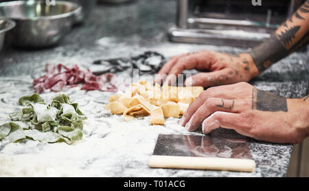 Recette de famille. Photo en gros plan des mains du chef des hommes avec des tatouages de finition pâtes italiennes sur la table de la cuisine avec de la farine. Cuisson Banque D'Images