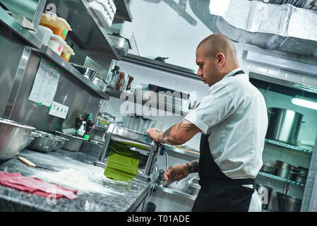 Des plats italiens traditionnels. Vue latérale du beau le roulement d'un chef de la pâte verte par machine à pâtes dans la cuisine. Cuisson Banque D'Images