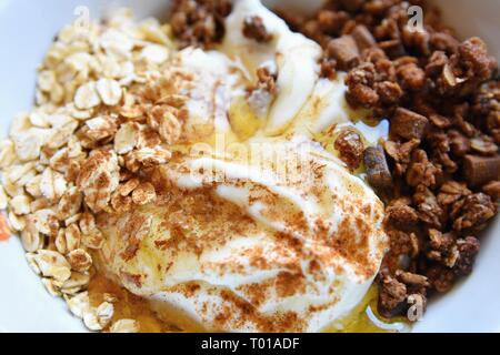 Des aliments sains - petit-déjeuner dans une assiette blanche. Muesli, yaourt, du gruau avec le chocolat, le miel et la cannelle. Banque D'Images