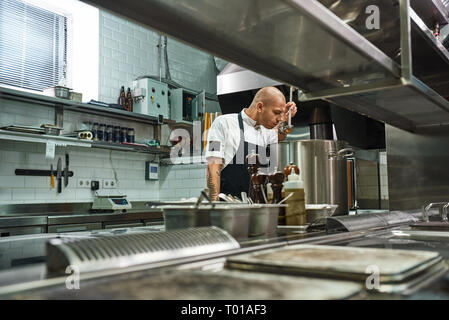 Ma fameuse soupe. Vue latérale du chef en tablier avec des tatouages sur ses bras sentir une soupe dans un restaurant cuisine. Concept de cuisine Banque D'Images