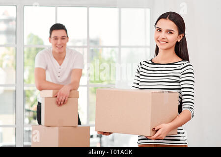 Jeune couple d'entrepreneurs indépendants, vendeurs, préparer le produit, boîte à colis pour la livraison au client. Femme en carton et regardant la caméra, tandis que l'homme debout près de la pile de boîtes dans l'arrière-plan. À l'intérieur, intérieur lumineux. Vente en ligne, e-commerce concept Banque D'Images