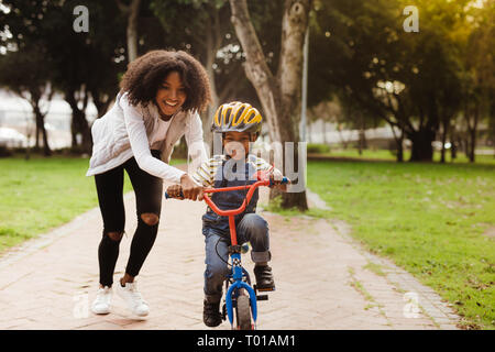 Happy cute boy apprendre à faire du vélo avec sa mère. L'enseignement de mère fils de circuler à bicyclette à parc. Banque D'Images