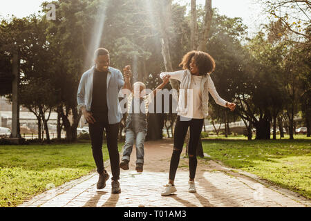 Heureux belle famille de trois walking in park. Couple heureux en profitant de l'extérieur de l'humeur ludique avec leur enfant. Banque D'Images