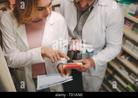 Chimiste femelle avec prescription pointing at medicine fort chez un collègue de drug store. Pharmacie avec une prescription à bon médicament Banque D'Images