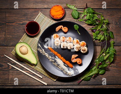 Délicieux rouleaux de sushi avec caviar et sésame sur la plaque noire servi sur la table en bois, décorées avec de l'avocat, des baguettes et des germes. Banque D'Images