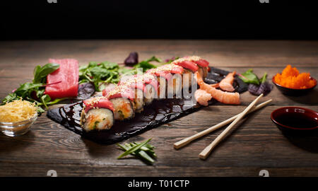 Rouleaux de sushi délicieux avec du riz et du poisson sur ardoise noire servi sur la table en bois, décoré avec des baguettes, bol de sauce soja caviar et les pousses. Banque D'Images