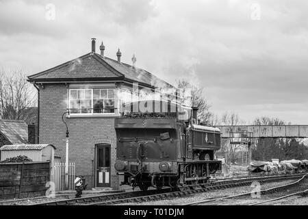 Vue arrière monochrome de la locomotive à vapeur britannique d'époque en action sur la ligne du patrimoine de Severn Valley Railway quittant la gare de Kidderminster par une boîte de signalisation. Banque D'Images