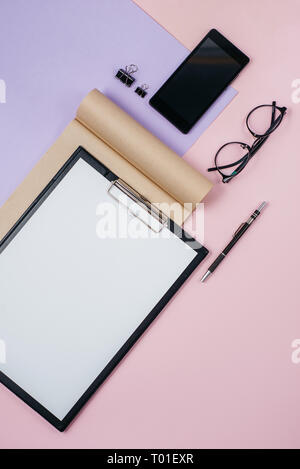 Des maquettes en blanc avec de l'espace de conseil clip, fournitures de bureau, stylo, bloc-notes, smartphone sur rose et violet. Mise à plat, vue du dessus, élégante femme c Banque D'Images