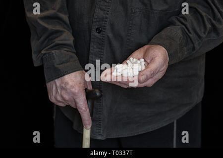 Un vieil homme avec une canne est titulaire d'une poignée de comprimés dans sa main, chemise noire, l'homme blanc Banque D'Images