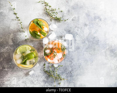 Boissons froides d'été jeu d'agrumes de différentes dans les verres sur un fond gris. Cocktail avec de pamplemousse, orange, citron-lime et de glace Banque D'Images