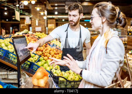 Beau d'aider les jeunes travailleurs en uniforme femme client pour peser sur la balance des pommes dans le supermarché Banque D'Images