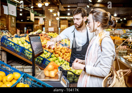 Beau d'aider les jeunes travailleurs en uniforme femme client pour peser sur la balance des pommes dans le supermarché Banque D'Images